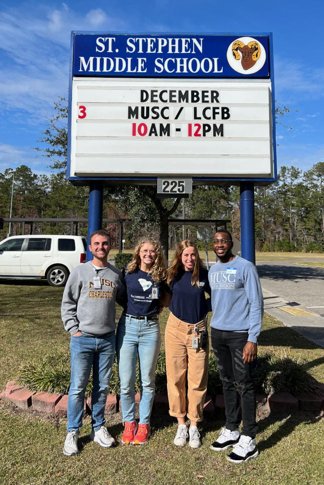 Four MUSC students in front of a sign advertising the MUSC CARES clinic.