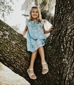 Young girl sitting in a tree smiling.