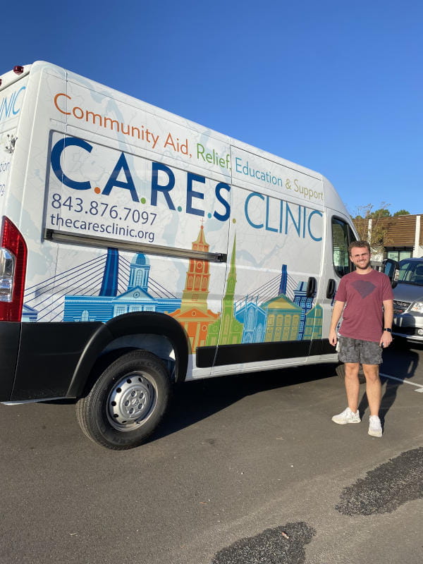 A medical student stands next to a van with the words CARES Clinic on the side. The van is used by the clinic for community outreach. 