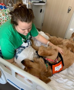 A young woman rests in a hospital bed, gently cradling a dog on her lap, showcasing a moment of comfort and companionship.