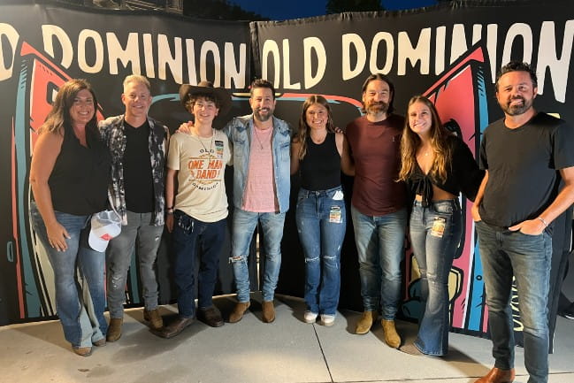 Members of the country band “Old Dominion” stand in front of a sign that reads "Old Dominion," smiling and posing for a photo with Brendan and his family.