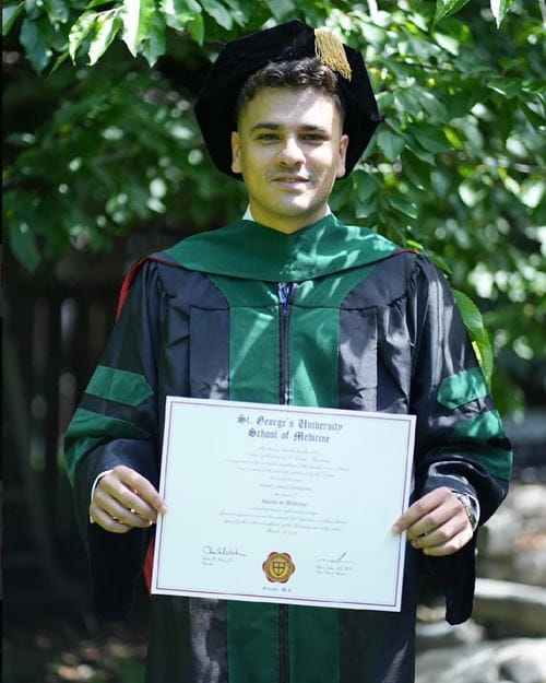 A man in a graduation gown proudly holds his diploma, celebrating his academic achievement.