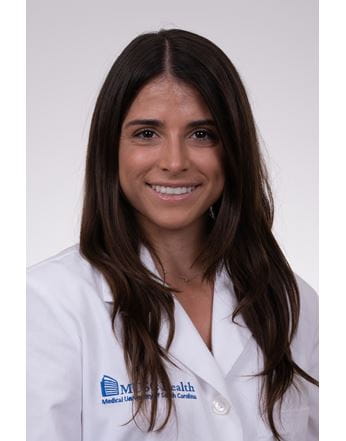  A woman smiling in a white medical lab coat with "MUSC Health Medical University of South Carolina" embroidered on it.