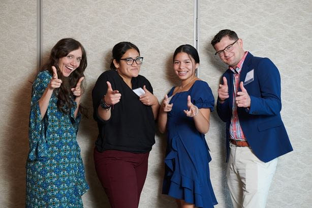 A group of four people happily posing together, each showing a thumbs up gesture for the picture. 