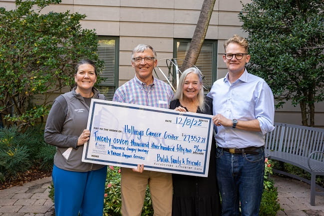 Four people stand together, holding a check that represents their contribution to a cancer charity.