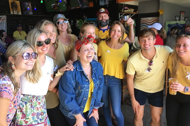 A lively group of friends dressed in yellow shirts and sunglasses, celebrating and having a great time outdoors.