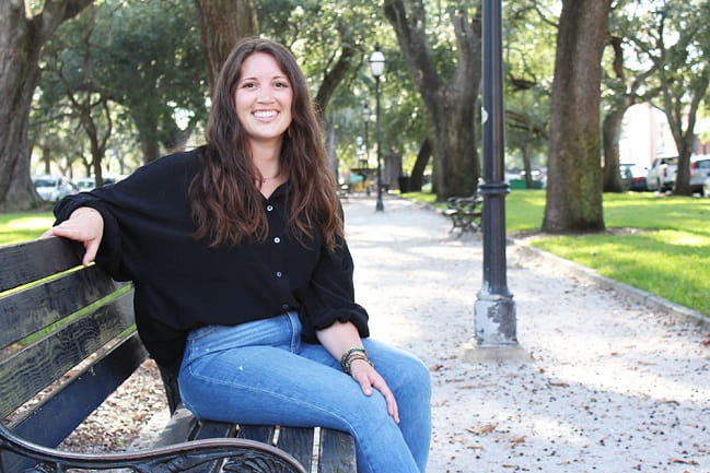 A woman sits on a park bench, surrounded by greenery, enjoying a peaceful moment in the park.